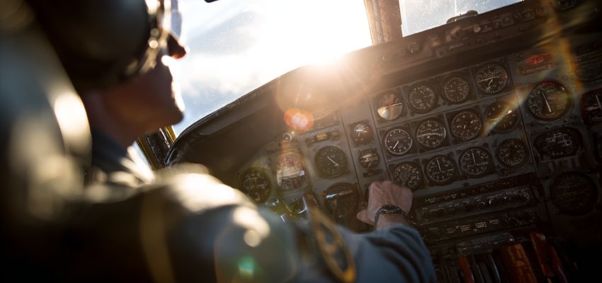 Pilot's hand on controls in aircraft cockpit with instrument panel visible, sunlight streaming in, illustrating slip vs skid coordination via turn indicator during flight.