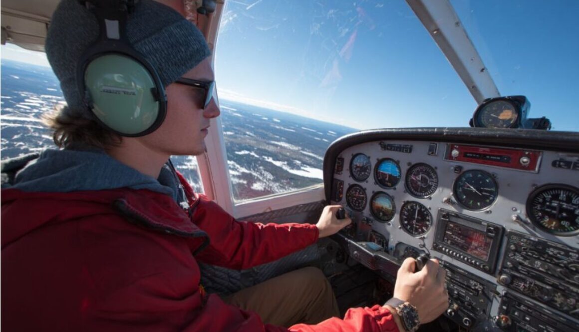 Pilot wearing headset and sunglasses operating controls in cockpit with scenic snowy landscape outside, showing hands-on management of slip vs skid using turn coordinator ball.